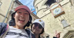 Carol and a friend take a selfie with a clock tower in the background
