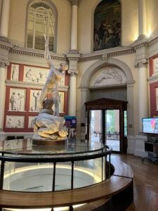 A marble statue sits on a round table in the center of a library.