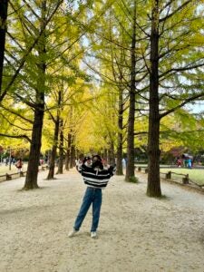 Nona poses in front of a forest of trees with bright, yellow leaves