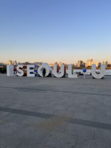 Nina sits on a giant display that reads, "I Seoul U"