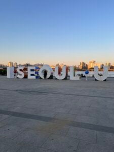 Nina sits on a giant display that reads, "I Seoul U"