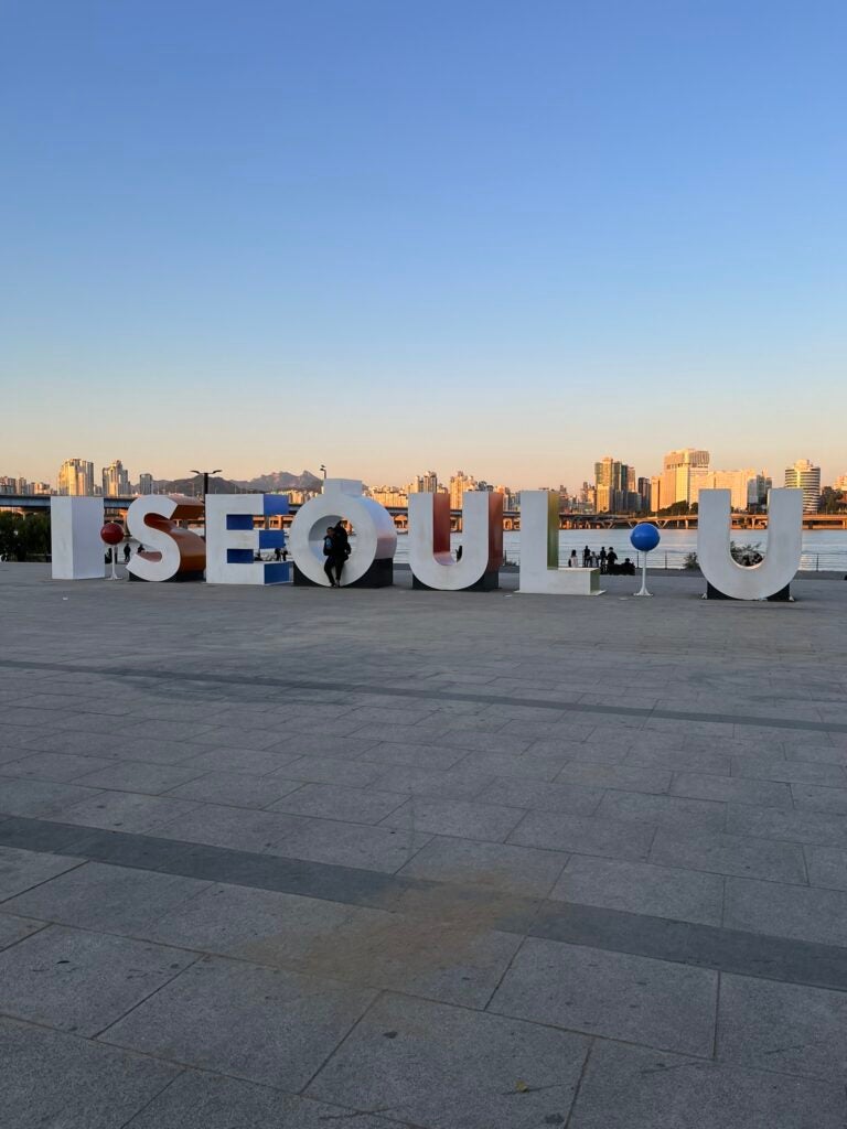Nina sits on a giant display that reads, "I Seoul U"