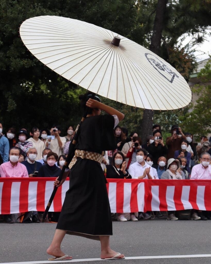 A person dressed in a traditional robe holds a white umbrella