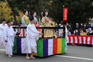 Three women dressed in traditional clothing and makeup sit on top of a parade float