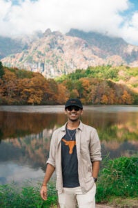 Sourav smiles in front of a lake with a mountain range in the distance