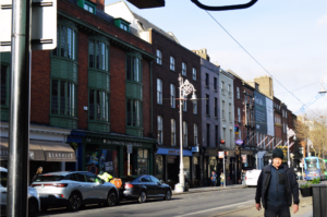 Brick buildings in Ireland with storefronts on the first floor off a main road. 