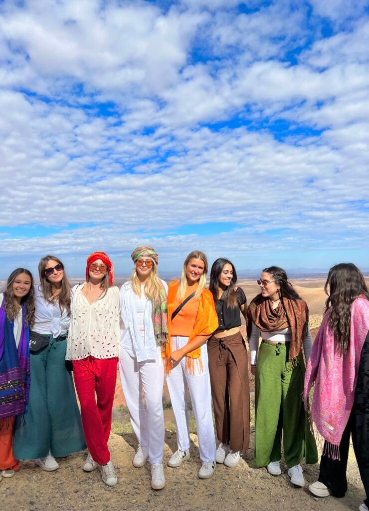 A group of eight students standing together, smiling and posing for a photo with a mountainous landscape in the background.