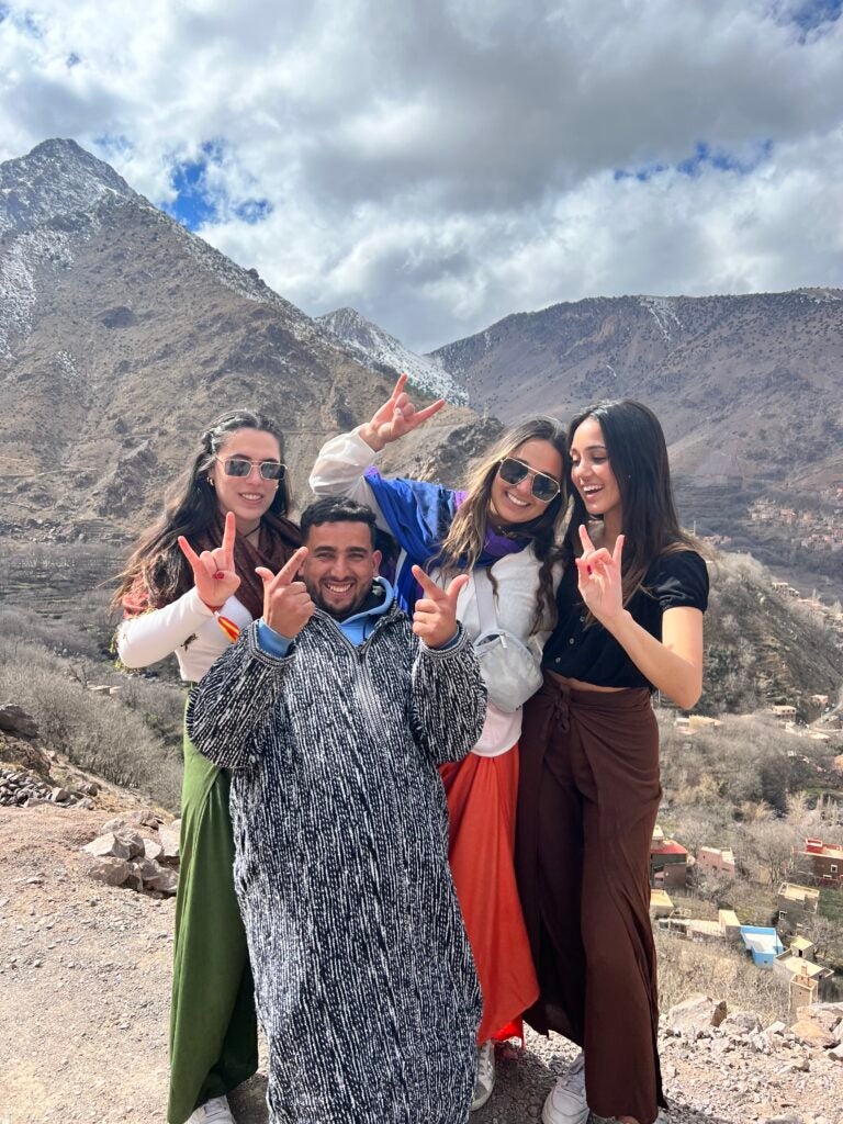 Four students surround their tour guide while posing for a photo with mountains in the background.