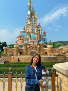 A student poses while leaning on a gate and in front of castle in Disneyland in Hong Kong