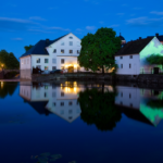 Night view of Uppsala, Sweden showing buildings and architecture along the waterfront of a lake, illuminated by building lights and reflections on the water