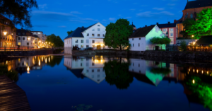 Night view of Uppsala, Sweden showing buildings and architecture along the waterfront of a lake, illuminated by building lights and reflections on the water