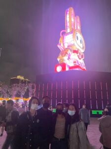 Four students posing for a photo at an outdoor, night festival with a large rabbit character glowing behind them.