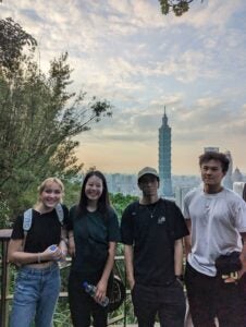 Four students posing in front of a tall, think building structure with a pointed tip in Taiwan