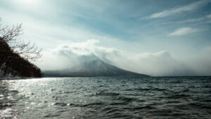 A mountain peak stands tall in the background as the sea waves naturally on a cloudy day.