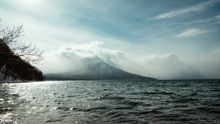 A mountain peak stands tall in the background as the sea waves naturally on a cloudy day.
