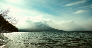 A mountain peak stands tall in the background as the sea waves naturally on a cloudy day.