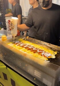 A person cooking food on a hot griddle at a night market street stall.