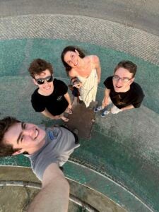 Four friends standing close to each other, smiling and taking a selfie with a smartphone.