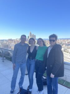 "Four friends standing together on a rooftop in Madrid on a sunny day posing for a photo, with big smiles on their faces.