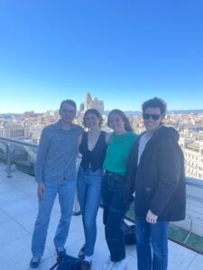 "Four friends standing together on a rooftop in Madrid on a sunny day posing for a photo, with big smiles on their faces.