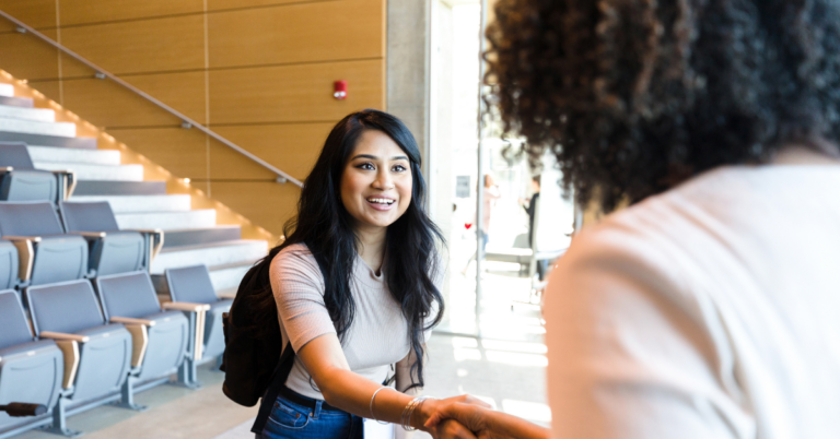 Student and professor shake hands in large classroom after class.