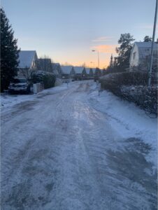  A winter scene of a neighborhood covered in snow with the sun peaking through clouds in the sky above.