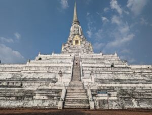 Student smiling and standing in front of Wat Phu KhaoThong, a large Buddhist temple in Thailand with many steps.