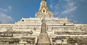 Student smiling and standing in front of Wat Phu KhaoThong, a large Buddhist temple in Thailand with many steps.