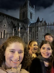 Four friends stand in front of a castle at night in Ireland. The castle towers above them with intricate stonework in the background.