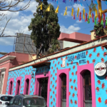 Bright building painted in blue and pink sits in the center of a neighborhood on a sunny day