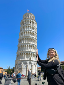 Student in black sweater and sunglasses poses as if she's keeping the leaning tower of Pisa from falling over