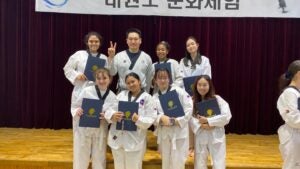 Students smiling while posing with taekwondo instructor while holding up certificates.