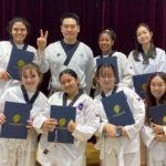 Students smiling while posing with taekwondo instructor while holding up certificates.
