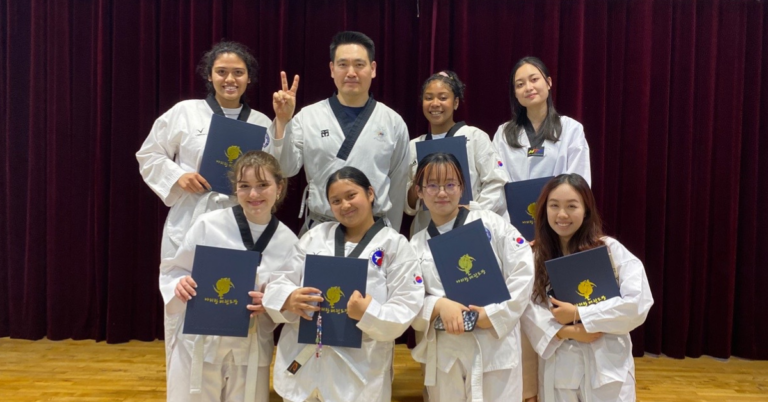 Students smiling while posing with taekwondo instructor while holding up certificates.