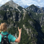 Woman on top of mountain with larger mountains in the background. Women holds up the "hook 'em" hand symbol which is synonymous with The University of Texas at Austin