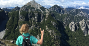 Woman on top of mountain with larger mountains in the background. Women holds up the "hook 'em" hand symbol which is synonymous with The University of Texas at Austin