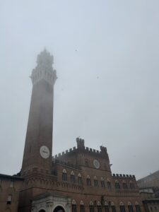 Clouds and fog cover the tower of a large stone building with a round clock.