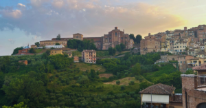 Mountains of Siena, Italy with stone churches and buildings behind a blue and yellow cloudy sky.