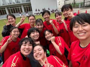 A group of female students pose for a selfie after a soccer game. The students are all wearing a similar red and black uniform.