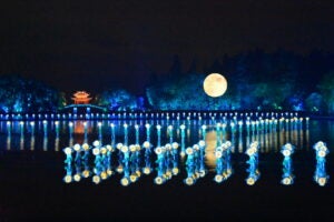 Blue floating lights on top of a river during a full moon.