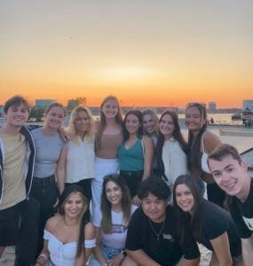 A group of friends pose for a photo near a waterfront. The sun is setting a serene orange.