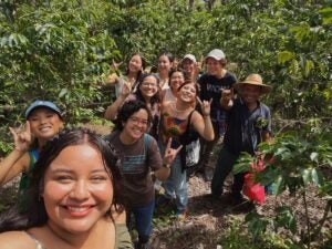 A group of about 10 people take a selfie and smile at the camera. The sun is shinning bright and there is slight precipitation on the faces of each group member.