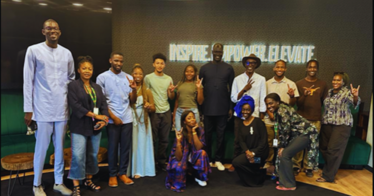 A group of students smile while posing for a group photo in front of a wall that reads "inspire. empower. elevate."