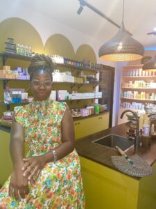 A young lady in a colorful yellow floral dress with glasses and a bun poses for a photo inside a beauty shop.