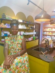 A young lady in a colorful yellow floral dress with glasses and a bun poses for a photo inside a beauty shop.