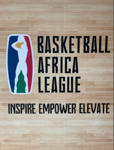 The Basketball Africa League's logo on the wooden floor shows a silhouette of a person making a jump shot behind blue, red, and green colors. The slogan, "inspire empower elevate" is below the image and name of the logo.