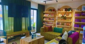 The interior of a beauty shop is decorated in bold colors of green, yellow, bring pink, aqua and shades of brown. There are beauty products on display on a wall.