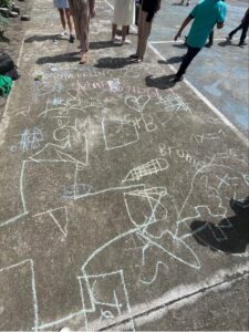 Chalk drawings from children are displayed on the concrete of an open schoolyard