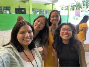 A group of students smile for a photo inside a school building after successfully completing their first day as student teachers