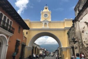 A grand yellow and white archway on a busy street in Guatemala.